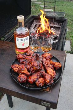 barbecue chicken wings on a plate next to two wine glasses and a bottle of bourbon