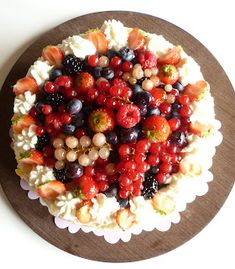 a cake covered in berries and other fruits on top of a wooden platter with white icing