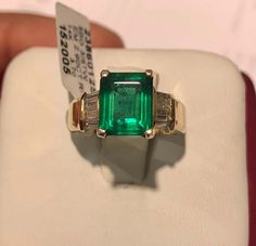 an emerald and diamond ring is displayed on a white box with a price tag in the background