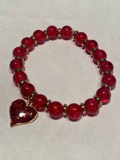 a red beaded bracelet with a gold heart charm on it's clasp closure