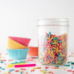 colorful sprinkles in a jar next to cupcake liners