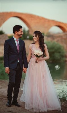 a man and woman holding hands while standing next to each other in front of a bridge