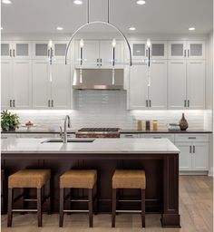 a large kitchen with white cabinets and counter tops, lights hanging from the ceiling over the island