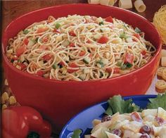 a red bowl filled with pasta and vegetables on top of a table next to other plates