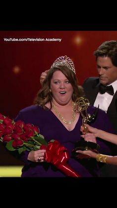 a woman in a purple dress holding flowers and an award