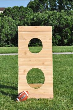 a football is sitting in the grass next to a wooden board with holes cut into it