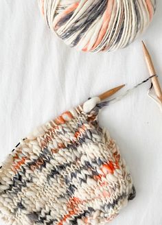 two balls of yarn and a knitting needle on a white surface, with one ball of yarn in the foreground