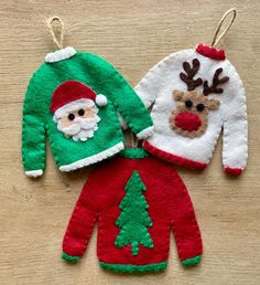 two christmas sweaters hanging from strings on a wooden table with santa clause and reindeer