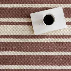 a cup of coffee sitting on top of a table next to a white and brown striped rug