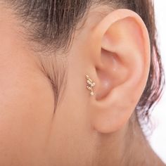 a close up of a person wearing a gold earring with small leaves on it