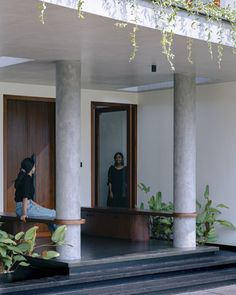 two people standing in the doorway of a house with large columns and plants on either side