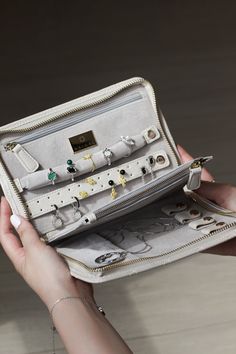 a woman's hand holding an open white purse with jewelry on the front and inside