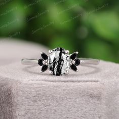 a black and white ring sitting on top of a piece of cloth with green leaves in the background