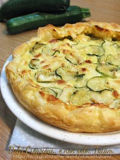 a pizza with zucchini and cheese is on a plate next to a cucumber