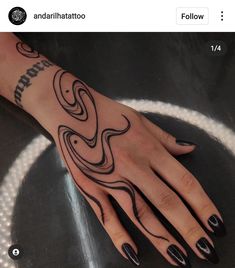 a woman's hand with black nail polish and tattoos on her left arm, sitting on a table