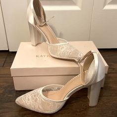 a pair of white high heel shoes sitting on top of a box next to a door