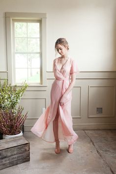 a woman standing in front of a window wearing a pink dress