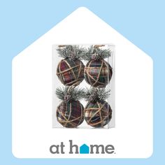 three plaid ornaments in a clear box with pine cones on the top and at home logo below