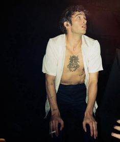 a man with tattoos on his chest standing in front of a black background wearing a white jacket