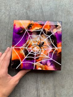 a hand is holding up a small painting with a spider on it's web