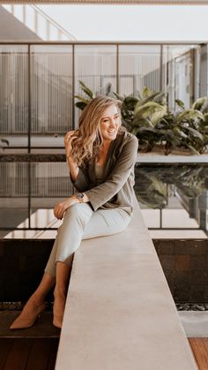 a woman sitting on top of a cement bench next to a plant filled pool in an office building