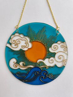 a blue and gold plate with clouds, sun and water in the center on a chain