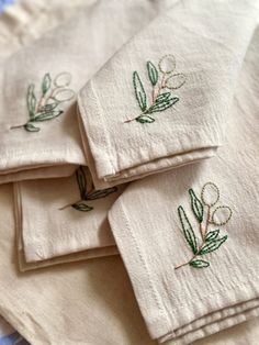 four embroidered napkins on top of each other with green leaves and flowers in the middle