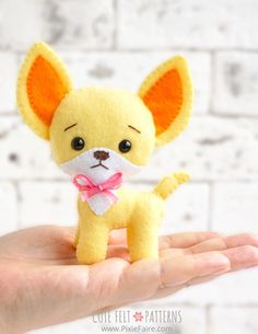 a hand holding a small yellow dog with a pink bow