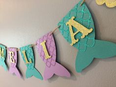 some little mermaid decorations are hanging on the wall with their name spelled out in gold and green