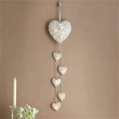 a white heart hanging on the wall next to a candle and vase with flowers in it