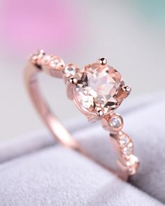 a ring with an oval shaped morganite surrounded by small white diamonds on a cushioned surface