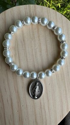 a white bracelet with a silver saint medal on it and a wooden plaque in the background