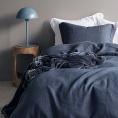 a bed with blue linens and pillows on the floor next to a night stand