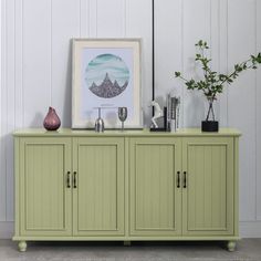 a green sideboard with two vases and a painting on the wall behind it