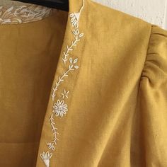 the back of a yellow dress with white embroidered flowers on it's chest and shoulders