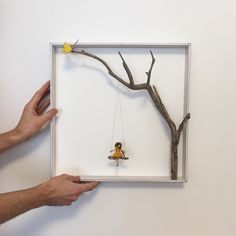 two hands are holding a shadow frame with a toy girl on a swing hanging from a tree branch