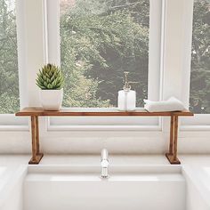 a white sink sitting under a window next to a wooden shelf with a succulent plant on it