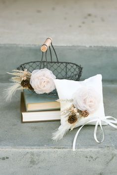 two flowers are sitting on top of some books and a basket with pine cones in it