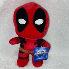 a deadpool stuffed animal is sitting on a white blanket with an universal studios sticker