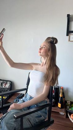 a woman sitting in a chair holding up a cell phone