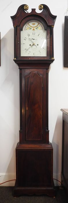 an old grandfather clock sitting on top of a wooden stand in front of a wall