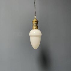 an old fashioned light hanging from a chain on a gray wall with a white lamp shade