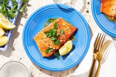 two blue plates topped with food next to silverware and lemon wedges on a table