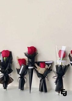 five red roses are in black vases with ribbons tied around them and placed against a white wall