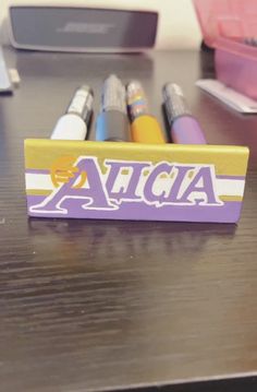 some pens are sitting on top of a wooden table with the word alcia written in purple