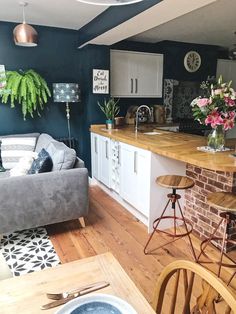 a living room filled with furniture next to a kitchen and dining room table in front of a brick wall