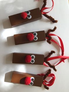 three brown paper tubes with reindeer noses and red ribbon tied around them on a white surface