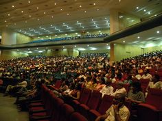 an auditorium full of people sitting in red chairs