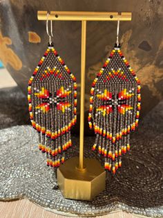 a pair of beaded earrings is displayed in front of a metal stand on a table