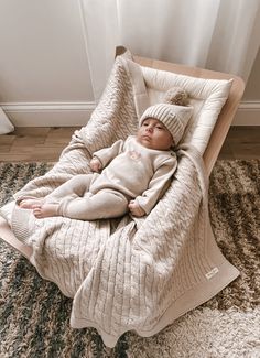 a baby is sleeping in a beanie on a chair with a blanket over it